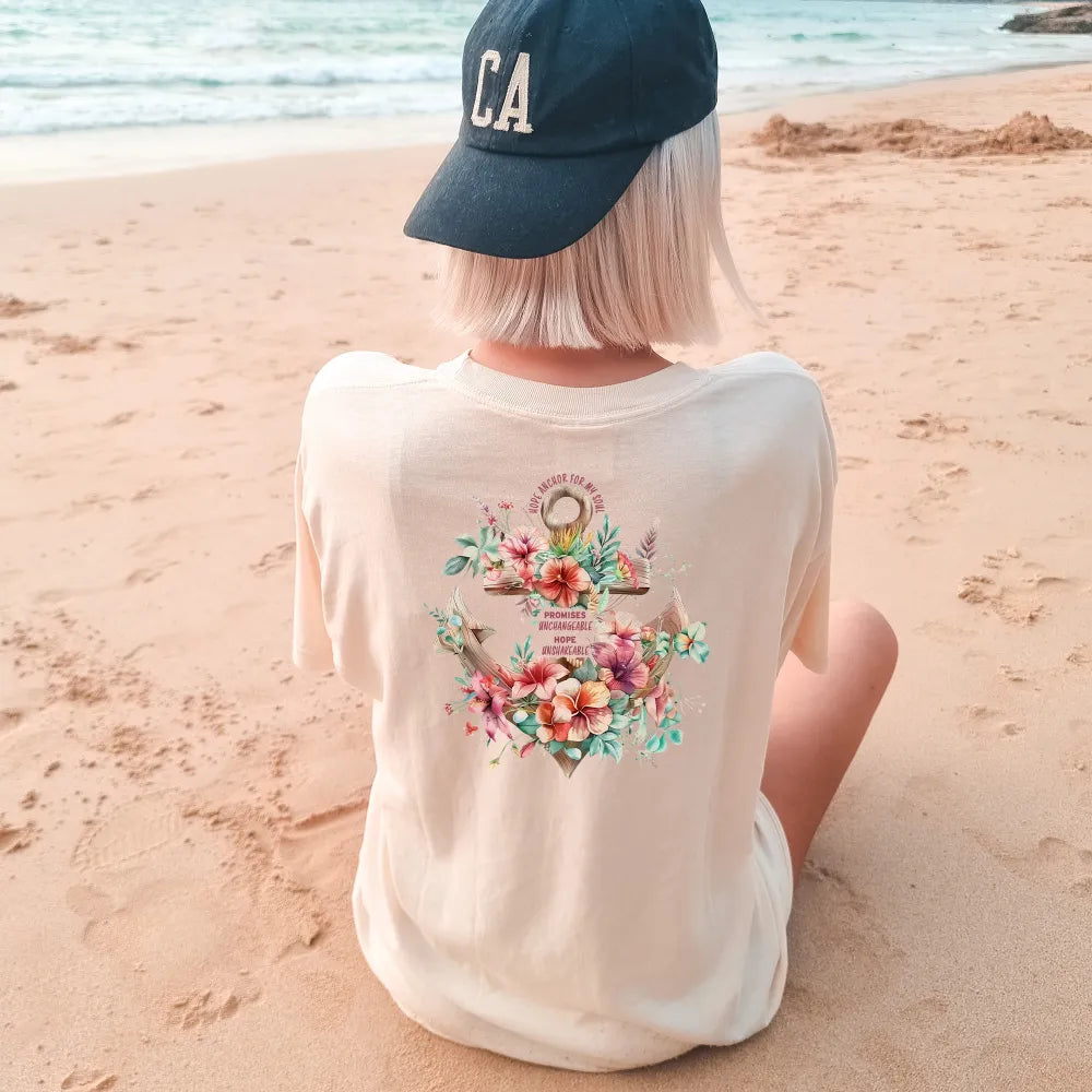 Person sitting on the beach looking at the sea, wearing a cap and a Be Still and Know Hope Anchor Floral Shirt with Hawaiian flowers.