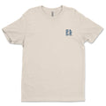 Plain beige Be Still and Know Hope Anchors shirt with a small blue logo on the left chest, symbolizing eternal hope.