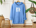 A Coastal Calm Hoodie In Carolina Blue with the word bk and BSAK Logo on it, by the brand Be Still and Know.