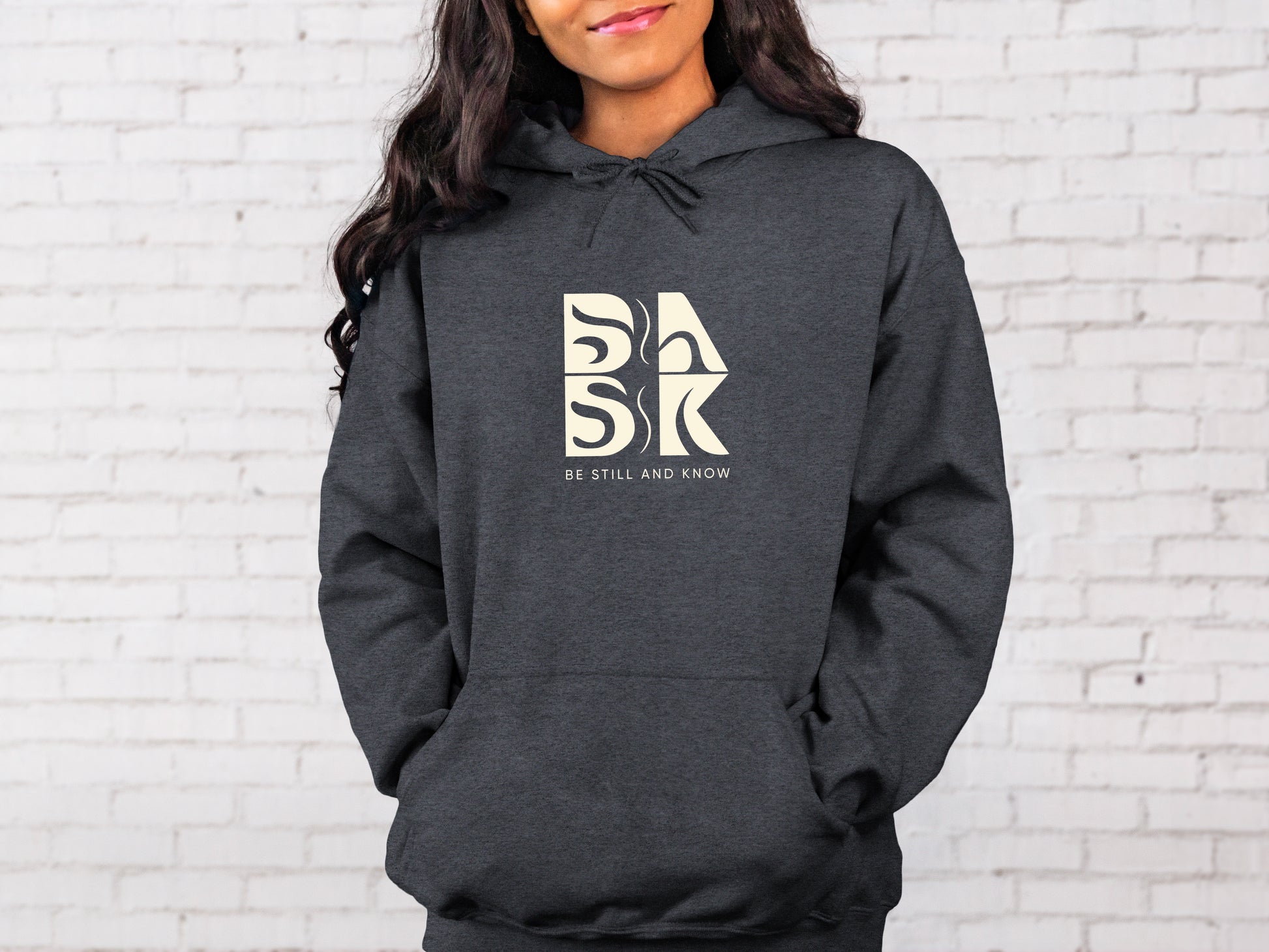 A woman wearing a Blessed Beginnings Hoodie In Dark Heather with the Be Still and Know logo, representing Christian Apparel.