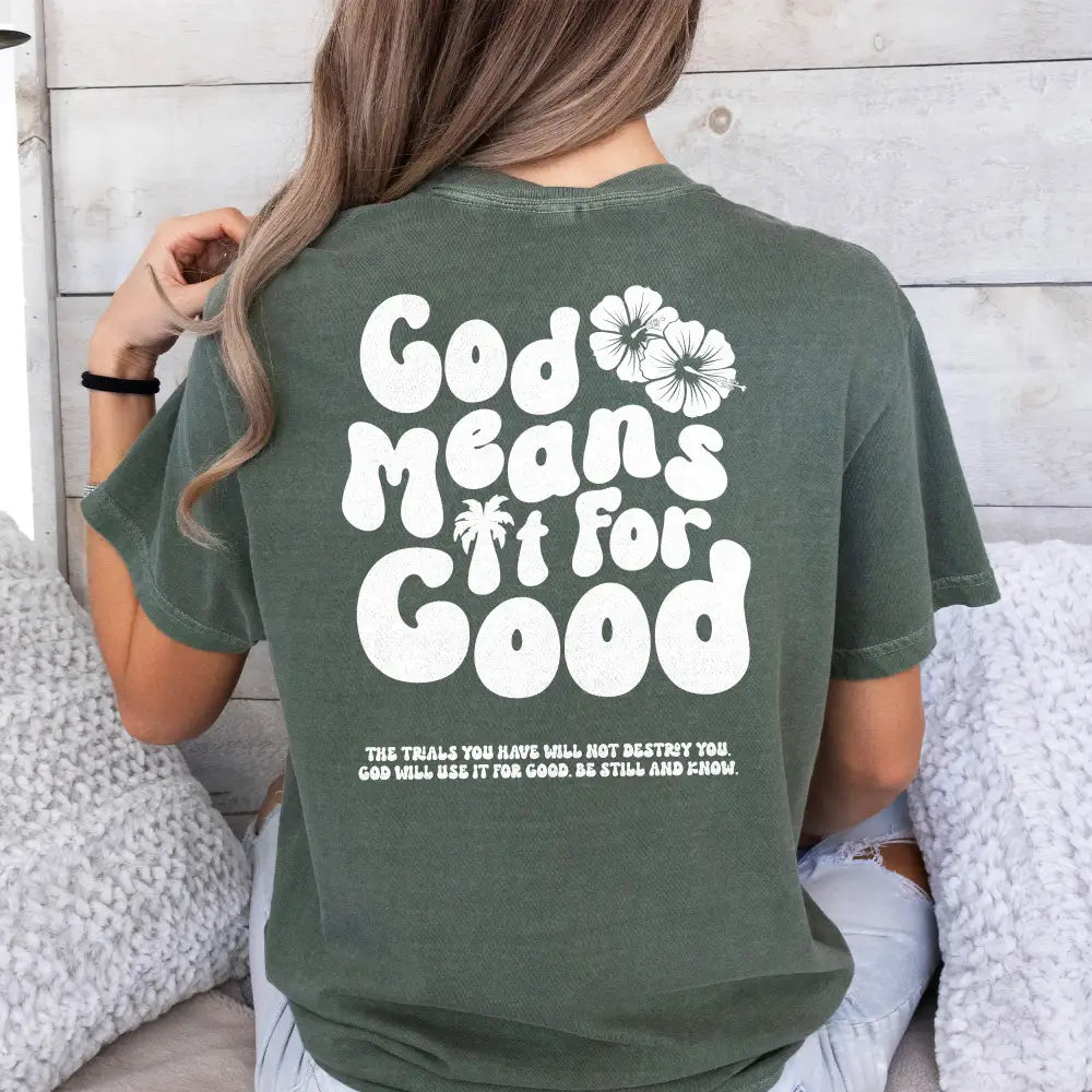 A person from behind wearing a Be Still and Know God Means It For Good Shirt in green with the phrase "God grows new life" printed in white letters, accompanied by a small design of a flower.