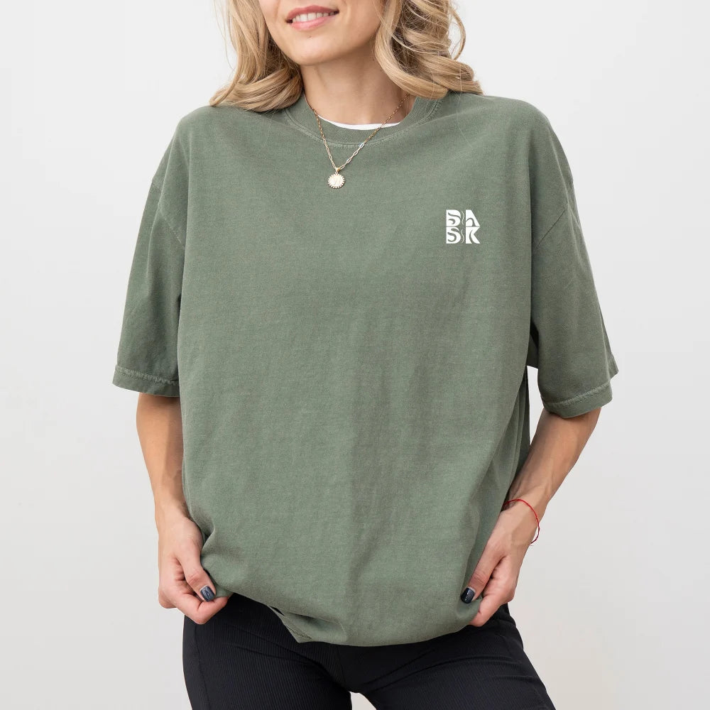 Woman experiencing unshakeable joy wearing a green oversized Be Still and Know "God Means It For Good" shirt with a small white logo on the left chest.