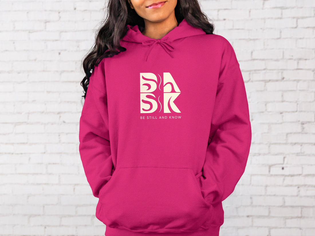 A Golden Coast Hoodie in Heliconia with the Be Still and Know logo on it.