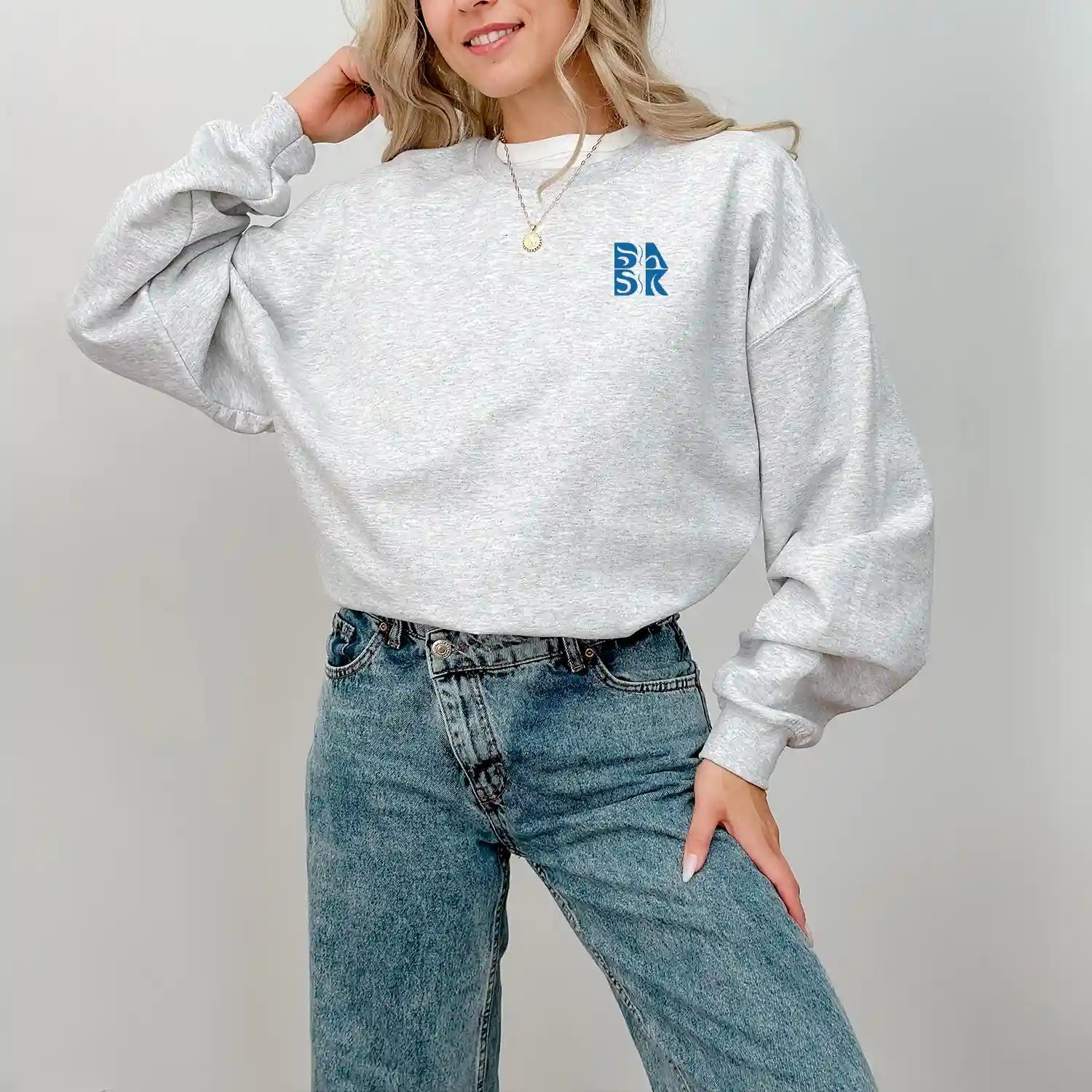 A woman, dressed in casual attire of a grey sweatshirt and jeans, proudly showcases her Be Still and Know Kupa'a Tide Sweatshirt.