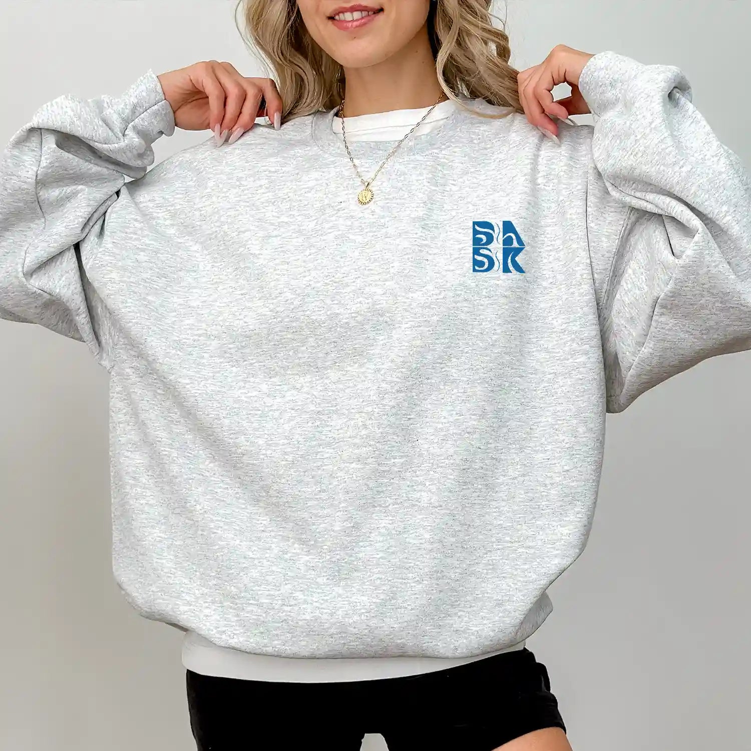A woman wearing a grey Kupa'a Tide Sweatshirt with a blue Be Still and Know logo on it.