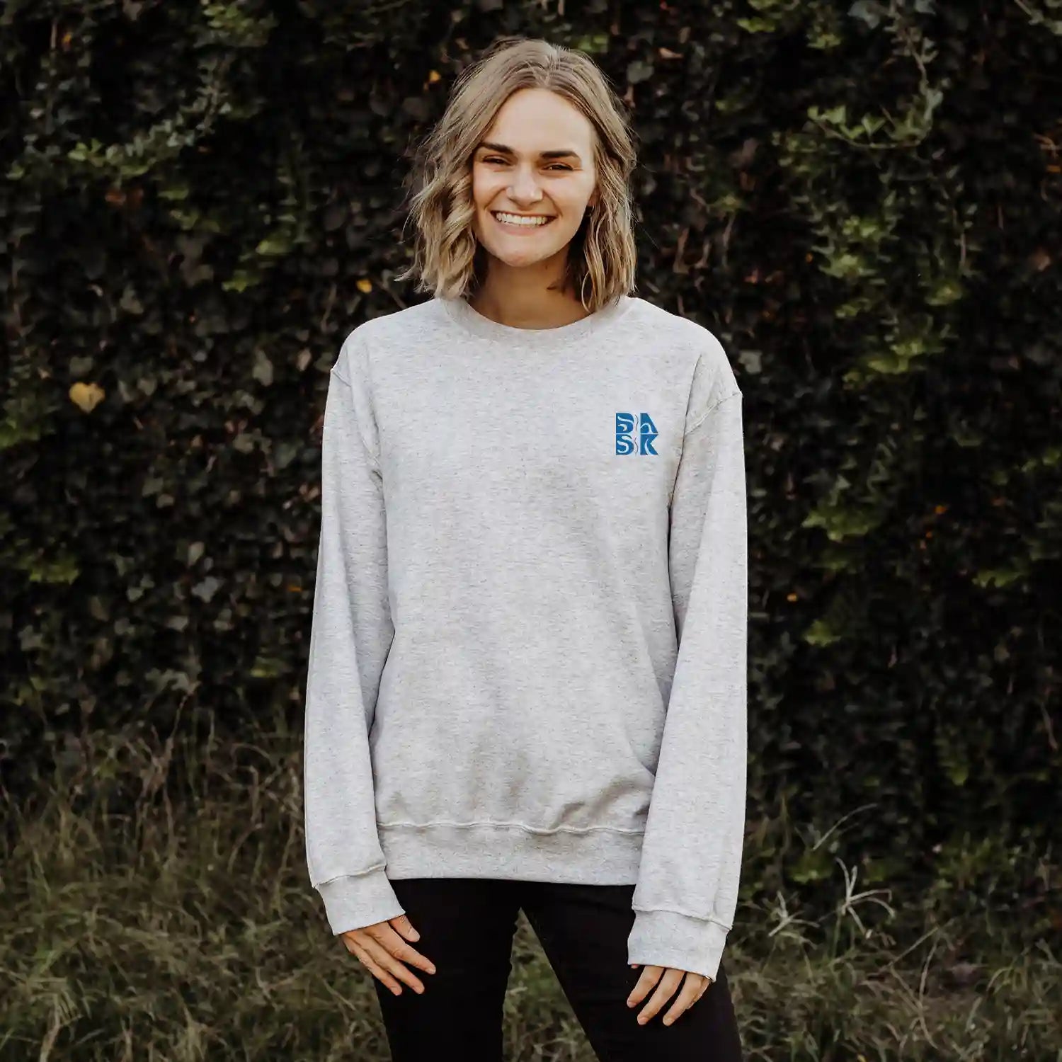 A woman wearing a grey Kupa'a Tide Sweatshirt with the Be Still and Know logo on it.