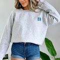 A woman wearing Christian apparel poses for a picture, showcasing the Be Still and Know logo on the Kupa'a Tide Sweatshirt.