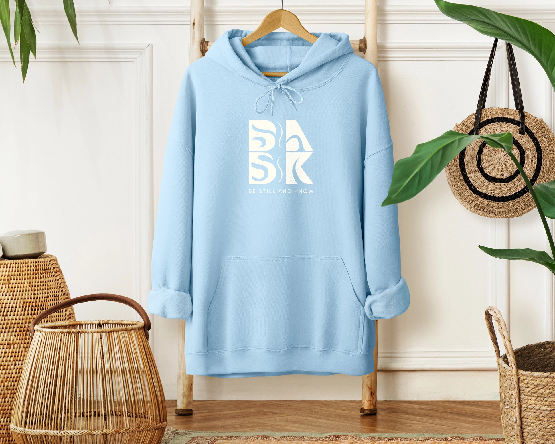 A Coastal Calm Hoodie in Light Blue with the Be Still and Know logo on it.