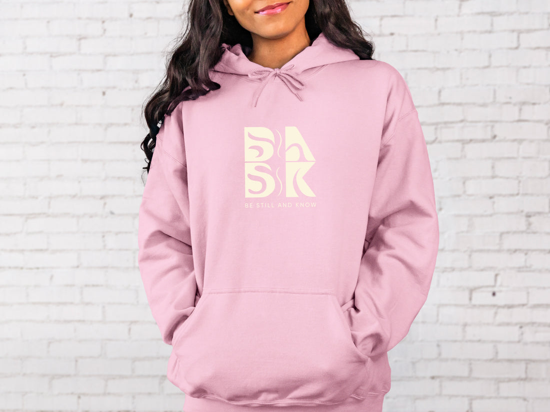 A Coastal Calm Hoodie In Light Pink with a Be Still and Know Logo on it.