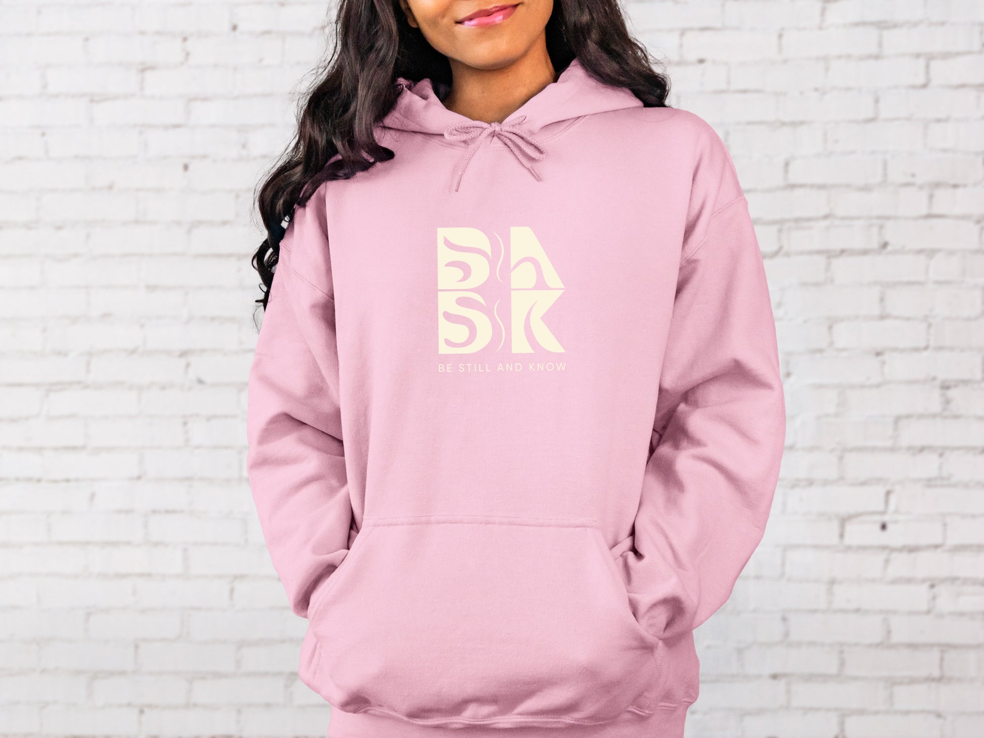 A woman wearing a Coastal Calm Hoodie in Light Pink by Be Still and Know, showcasing unique Christian Apparel.