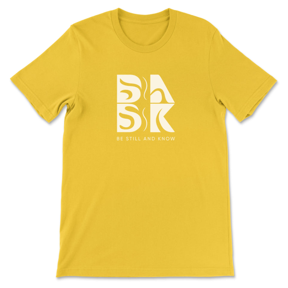 A Golden Coast Tee In Maize Yellow with the Be Still and Know logo on it.