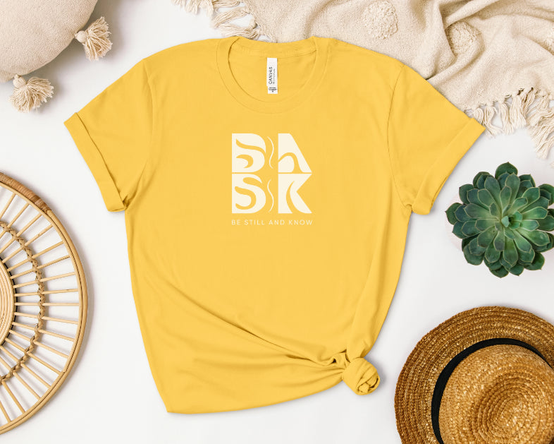 A Golden Coast Tee In Maize Yellow with the word "bak" and the BSAK logo, perfect for Christian apparel by Be Still and Know.