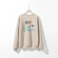A beige Nalu o ka Mana (Waves of Faith) sweatshirt with a palm tree and waves, featuring the Be Still and Know logo.