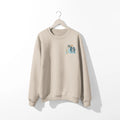 A beige Nalu o ka Mana (Waves of Faith) sweatshirt with a blue and white owl on it, featuring the Be Still and Know logo.