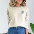 A woman wearing a Nalu o ka Mana (Waves of Faith) Sweatshirt from the brand Be Still and Know logo and jeans.