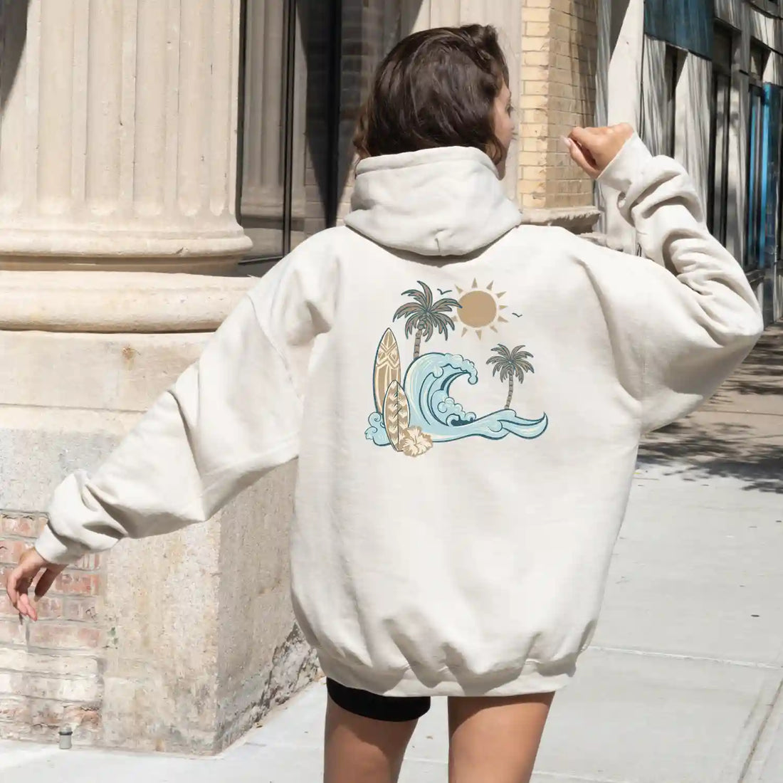 A woman wearing a Be Still and Know Nalu o ka Mana (Waves of Faith) Hoodie with an image of palm trees.