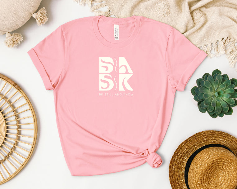 A Coastal Calm Tee in Pink with the Be Still and Know logo prominently displayed.