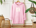A Coastal Calm Hoodie In Light Pink with the Be Still and Know logo on it.