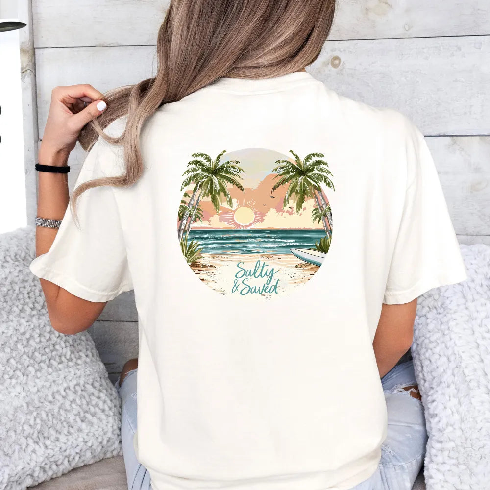 A woman sitting on a couch, seen from behind, wears a white Be Still and Know T-shirt featuring a tropical beach scene graphic with the text "salty & soaked.