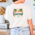 A woman wearing a Be Still and Know Salty & Saved Shirt with a tropical beach design and the names 