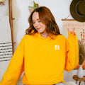 A cozy woman wearing a yellow Sunkissed & Saved Hoodie by Be Still and Know.