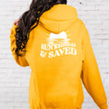 A woman wearing a yellow Sunkissed & Saved Hoodie from Be Still and Know that says 