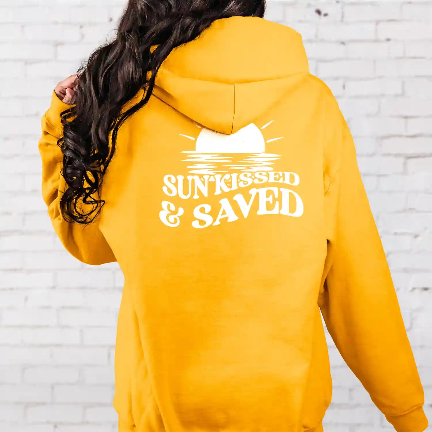 A woman wearing a yellow Sunkissed & Saved Hoodie from Be Still and Know that says "sunstruck" and "faith saved".