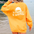 A woman wearing a Sunkissed & Saved Sweatshirt by Be Still and Know with the word 
