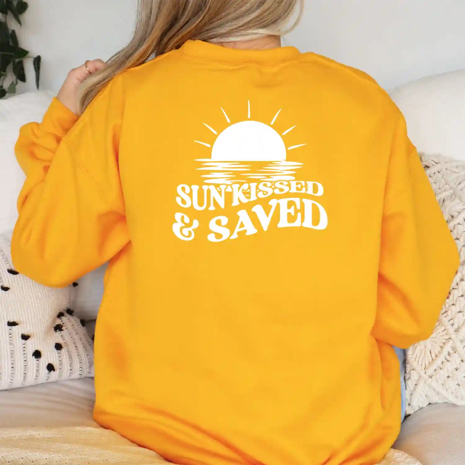 A woman wearing a Sunkissed & Saved Sweatshirt by Be Still and Know that exudes warmth and faith with the phrase "sun kissed" displayed.