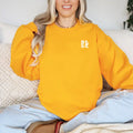 A woman wearing a Sunkissed & Saved Sweatshirt from the brand Be Still and Know, finding warmth and comfort on a couch.