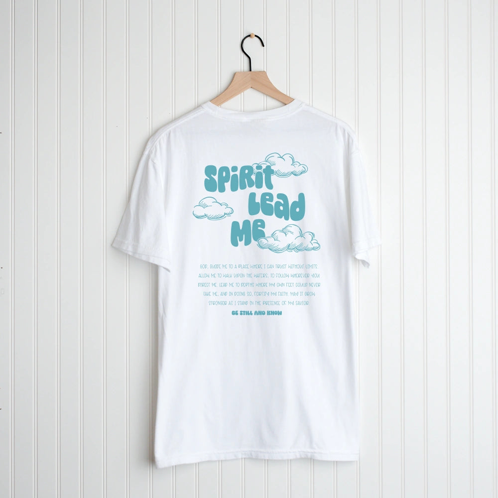 White Spirit Lead Me Shirt from Be Still and Know with "Spirit Lead Me, trust in Savior" text and cloud graphics hung on a wooden hanger against a white wooden background.