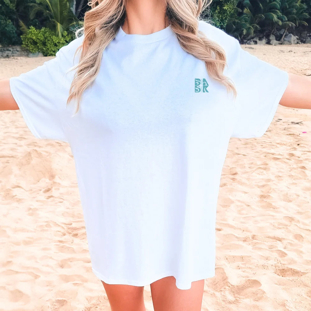 A person standing on the beach wearing a white "Spirit Lead Me Shirt" by Be Still and Know with the text "Spirit Lead Me: Trust in Savior" and additional text underneath.