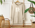 A beige Coastal Calm Hoodie In Sand with the Be Still and Know logo on it for Christian apparel.