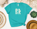A Aloha Maluhia In Teal t-shirt with the Be Still and Know logo on it.