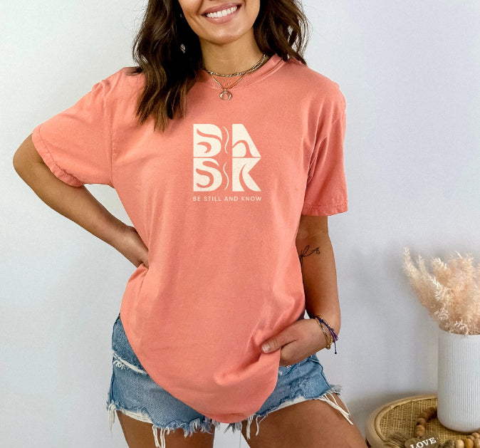 An Aloha Tee In Terracotta with the word "bak" on it, showcasing the Be Still and Know logo.