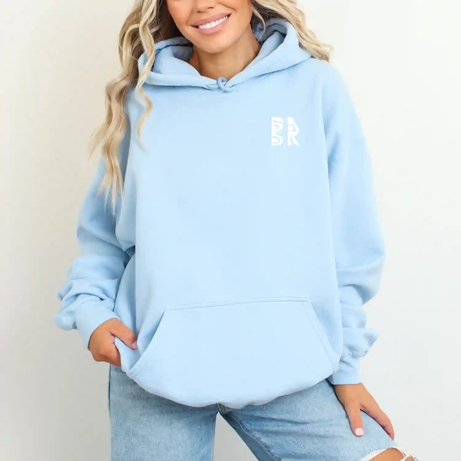 A woman wearing a Water Walking Faith Hoodie by Be Still and Know and jeans adorned with the BSAK Logo.