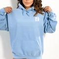 A woman wearing a blue Water Walking Faith Hoodie with a Be Still and Know Logo on it.