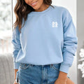 A woman wearing a light blue Water Walking Faith Sweatshirt adorned with the Be Still and Know Logo, paired with jeans.