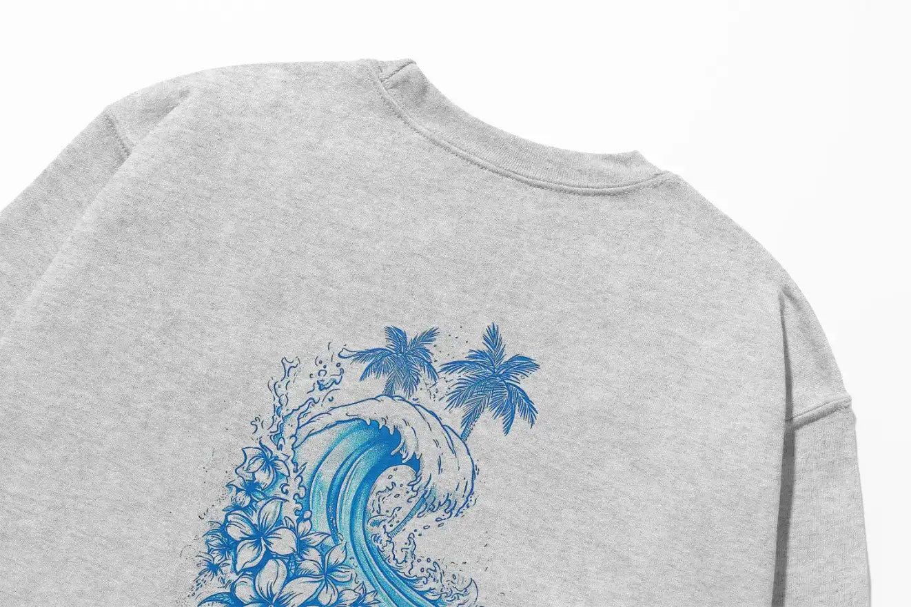 A grey Kupa'a Tide Sweatshirt with a blue wave and palm trees, featuring the Be Still and Know logo.